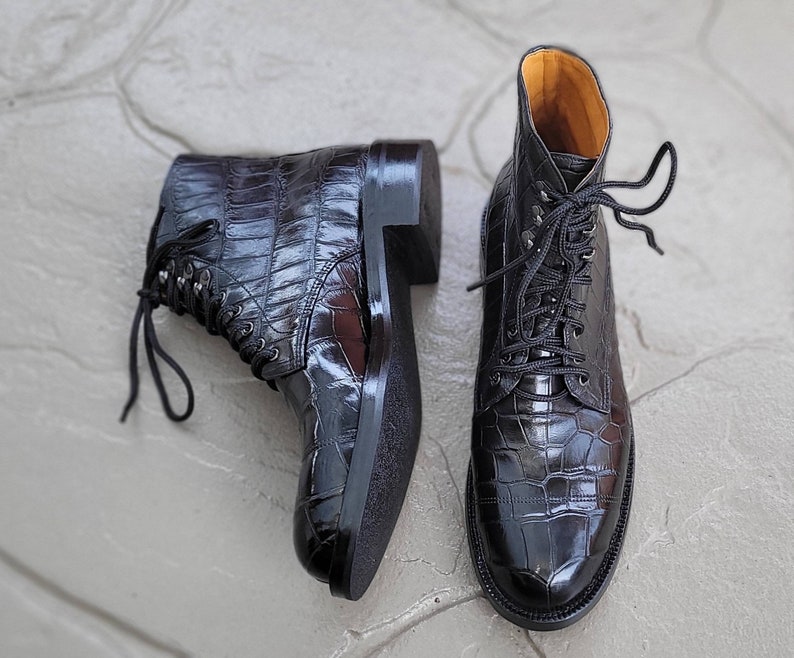 May include: A pair of black leather lace-up boots with a crocodile pattern. The boots have a pointed toe and a chunky heel.