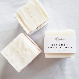 以下が含まれることがあります： 白い長方形の石鹸が2つ。1つは「Thompson Soap Co. Kitchen Soap Block, Soap | Savon 300 g」と書かれたラベルが付いている