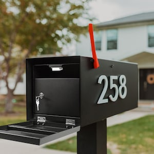 May include: A black mailbox with a red flag and the number 258 on the front. The mailbox has a keyhole and a small opening for mail.