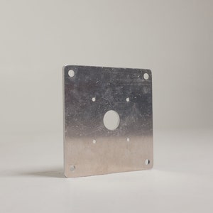 May include: A silver metal plate with a round hole in the center and four smaller holes around the edge.