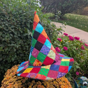 May include: A pointed hat constructed from a patchwork of multicolored fabric squares. The hat features a variety of patterns including polka dots, geometric shapes, and solid colors in shades of red, blue, green, orange, and purple.