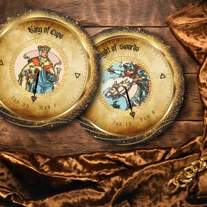 May include: Two decorative round wall art pieces featuring tarot card designs. One depicts the "King of Cups" and the other the "Knight of Swords." Both have a gold border and are set against a wooden background.