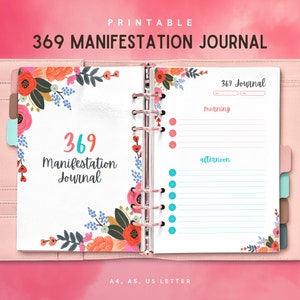 May include: A pink, open planner with a 369 Manifestation Journal design. The journal features floral accents, a ring binder, and sections for morning and afternoon entries. The cover and pages are white, with text in various colors.