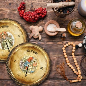 May include: An overhead shot of a wooden table with tarot cards, a wooden mouse figurine, a candle, and other mystical items. The tarot cards are round with gold rims and feature illustrations and text. A string of wooden beads and a small drum are also visible.