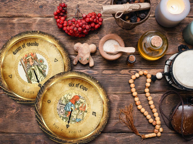 May include: An overhead shot of a wooden table with tarot cards, a wooden mouse figurine, a candle, and other mystical items. The tarot cards are round with gold rims and feature illustrations and text. A string of wooden beads and a small drum are also visible.