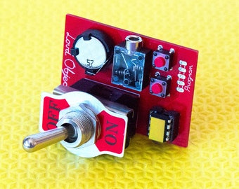 May include: A red circuit board with a silver toggle switch labelled "ON" and "OFF". The board has a small yellow component, a black component with a silver dial, and two red push buttons labelled "Program".