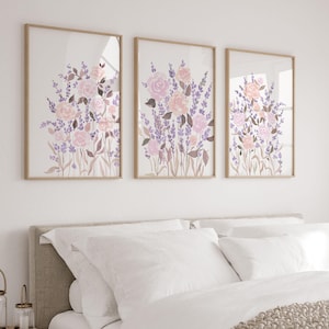 Può includere: Un letto bianco con una coperta di maglia beige e tre stampe floreali incorniciate sopra la testiera. Le stampe presentano fiori rosa e viola in stile acquerello.