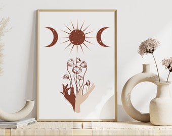 May include: A minimalist art print with a brown sun, two moons, and stylized hands holding flowers. The print is framed and displayed on a shelf with two vases and dried pampas grass.