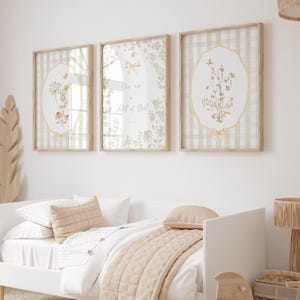 Op de afbeelding: Drie ingelijste wandkunstwerken met botanische illustraties en de tekst "You are a child of God". De kunst heeft een neutraal kleurenpalet met een ruitjesachtergrond. Een wit bed met beige beddengoed en kussens staat op de voorgrond.