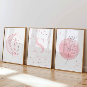 Può includere: Tre stampe incorniciate con uno schema di colori rosa e bianco. La prima stampa presenta una luna crescente con acquerello rosa e un motivo floreale. La seconda stampa presenta una lettera rosa "S" con uno sfondo ad acquerello rosa e una dispersione di stelle rosa. La terza stampa presenta un cerchio ad acquerello rosa con un motivo floreale e una dispersione di stelle rosa. La seconda stampa include anche il nome "Sina" in testo rosa.