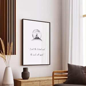 May include: A framed black and white print featuring a person meditating on a hill in front of a full moon. The text "Quiet the Mind and the soul will speak" is below the image. The print is displayed on a white wall.