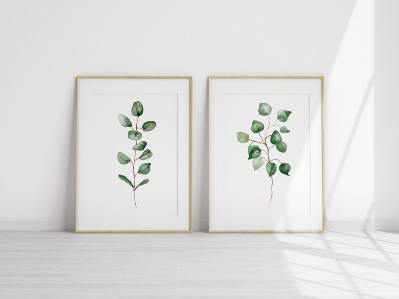 May include: Two framed watercolor prints of green eucalyptus branches on a white background. The frames are light wood.