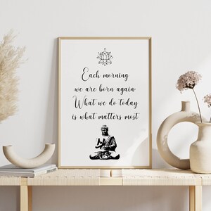 May include: A framed print with a black and white image of a meditating Buddha and the text "Each morning we are born again. What we do today is what matters most."