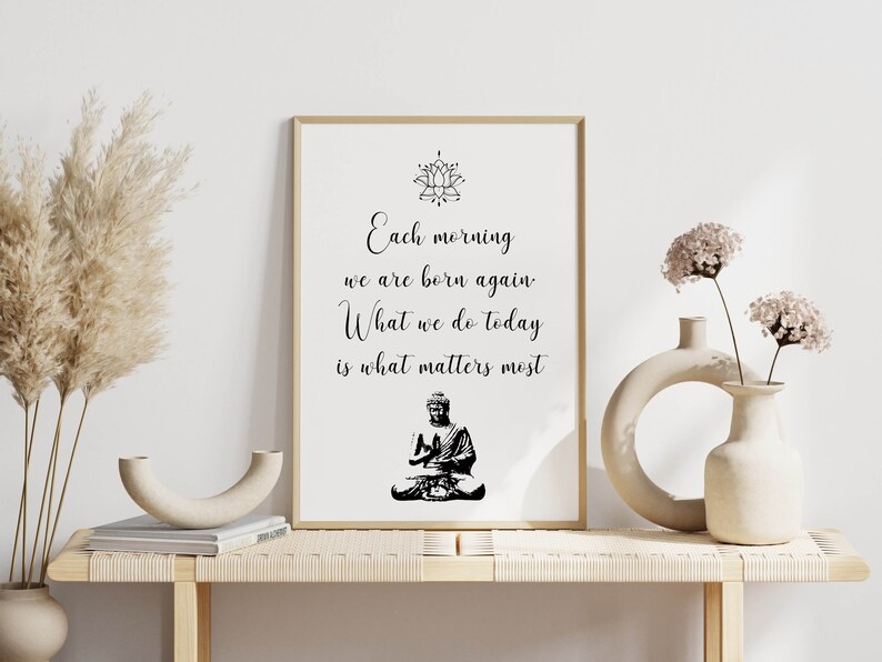 May include: A framed print with a black and white image of a meditating Buddha and the text "Each morning we are born again. What we do today is what matters most."