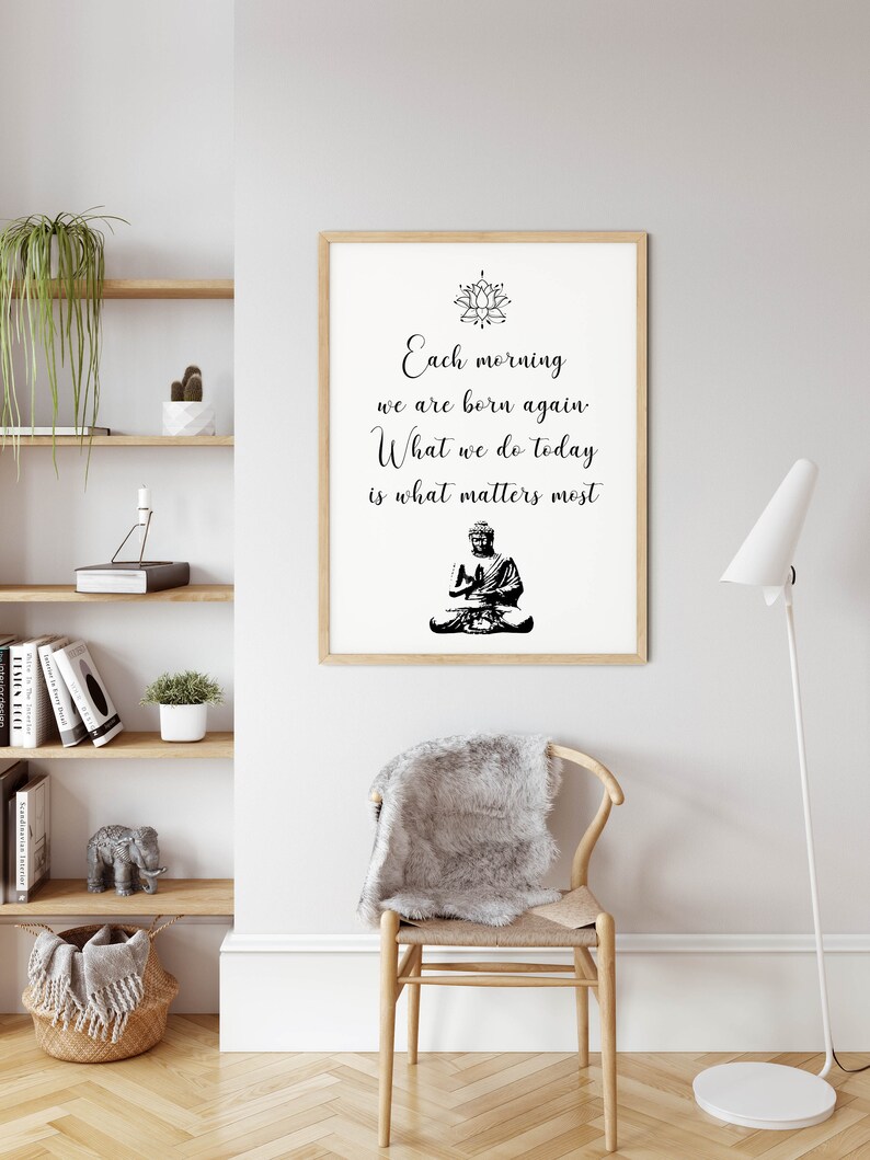 May include: A framed print with a black and white image of a meditating Buddha and a quote that reads "Each morning we are born again. What we do today is what matters most."