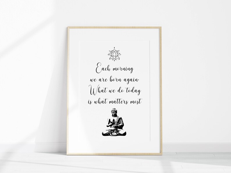 May include: A black and white printable wall art print with a quote that reads "Each morning we are born again. What we do today is what matters most." The quote is centered on a white background with a black lotus flower design at the top and a black silhouette of a meditating Buddha at the bottom.