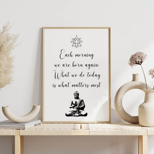 May include: A framed print with a black and white image of a meditating Buddha and the text "Each morning we are born again. What we do today is what matters most."