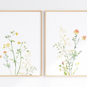 May include: Two framed watercolor prints of wildflowers. The print on the left features yellow and orange flowers with green stems and leaves. The print on the right features orange flowers with green stems and leaves.