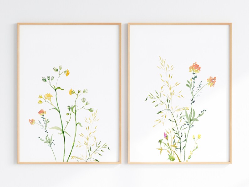 May include: Two framed watercolor prints of wildflowers. The print on the left features yellow and orange flowers with green stems and leaves. The print on the right features orange flowers with green stems and leaves.