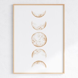 Pode incluir: Uma impressão emoldurada de uma ilustração de fases da lua em tons de marrom sobre um fundo branco.