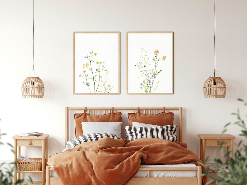 May include: Two framed watercolor prints of floral arrangements. The prints are hung on a white wall above a wooden bed with orange bedding. The prints are in a minimalist style with simple lines and muted colors.