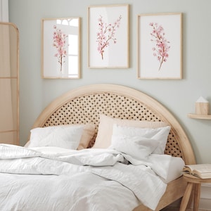 May include: A white bed with a light wood headboard featuring a woven rattan design. The headboard is curved and has a rounded top. Three framed prints of pink cherry blossoms hang above the bed.