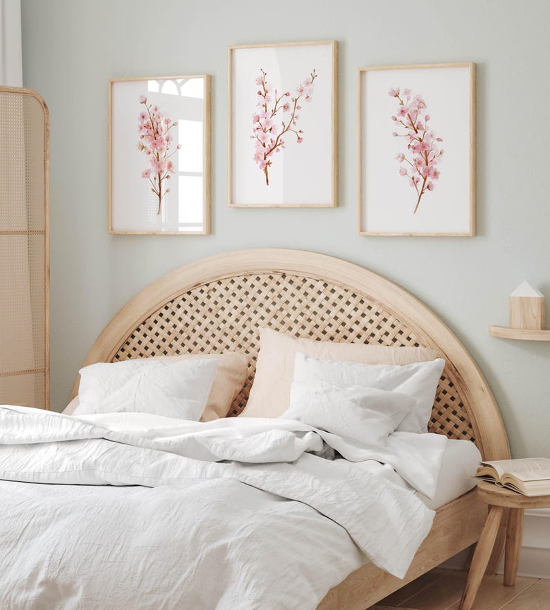 May include: A white bed with a light wood headboard featuring a woven rattan design. The headboard is curved and has a rounded top. Three framed prints of pink cherry blossoms hang above the bed.