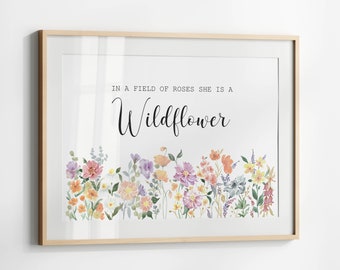 May include: A watercolor print with a white background featuring a floral border of colorful flowers and the text "In a field of roses she is a Wildflower".