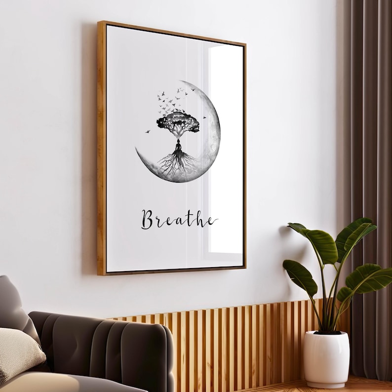 May include: Framed wall art featuring a black and white illustration. The artwork depicts a tree with roots and a person meditating within a crescent moon. The word "Breathe" is written in cursive below the image. The frame is gold.