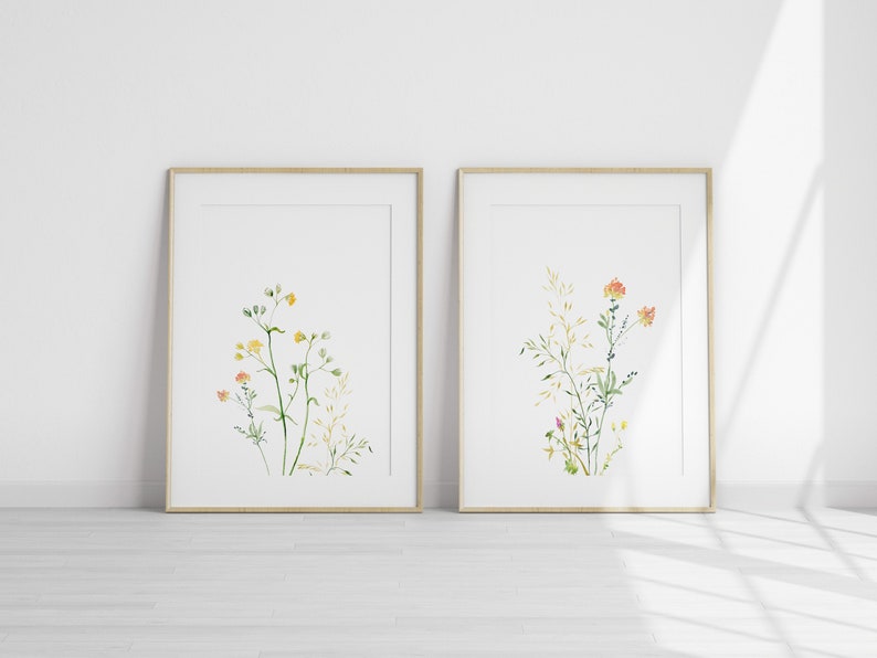 May include: Two framed watercolor prints of wildflowers. The print on the left features yellow wildflowers with green stems. The print on the right features orange wildflowers with green stems.