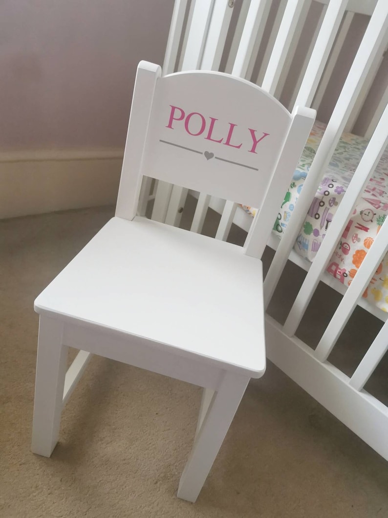 Pu&ograve; includere: Sedia in legno bianco con schienale arrotondato e il nome "POLLY" scritto in lettere rosa con un cuore grigio sopra il nome.