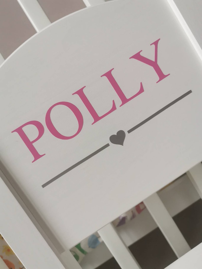Pu&ograve; includere: Testiera in legno bianco con il nome "POLLY" scritto in lettere rosa e un piccolo cuore grigio sotto il nome.