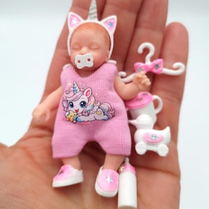 Peut inclure: Une poupée miniature vêtue d'un pyjama rose avec un motif de licorne, un bandeau en forme de corne de licorne et des chaussures roses. Accessoires : tétine, biberon, jouet en forme de canard, cintre et biberon. La poupée mesure environ 7.6 cm de haut.