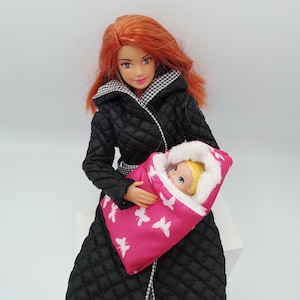 May include: A doll with red hair wearing a black quilted coat with a black and white checkered collar, holding a baby doll wrapped in a pink blanket with white butterfly designs. The baby doll has blonde hair and is wrapped in a white fur-lined hood.