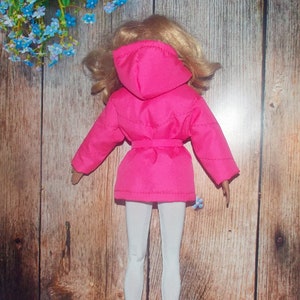 K&ouml;nnte beinhalten: Eine rosa Kapuzenjacke mit G&uuml;rtel und wei&szlig;er Hose. Die Jacke hat ein gestepptes Design und wird von einer Puppe getragen.