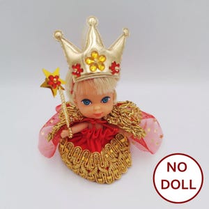 May include: A red and gold doll outfit with a crown, cape, and wand. The doll is wearing a red dress with gold trim and a gold crown with red and yellow flowers. The doll is holding a gold wand with a star on top.