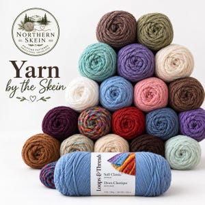 May include: A pyramid stack of various colored yarn skeins, including brown, green, purple, cream, blue, pink, and multicolored options. A single blue skein of Loops & Threads Soft Classic acrylic yarn is in the foreground with a label showing 7 oz.