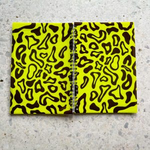 May include: A yellow notebook with a black and yellow abstract pattern on the cover. The notebook is closed and has a spiral binding.