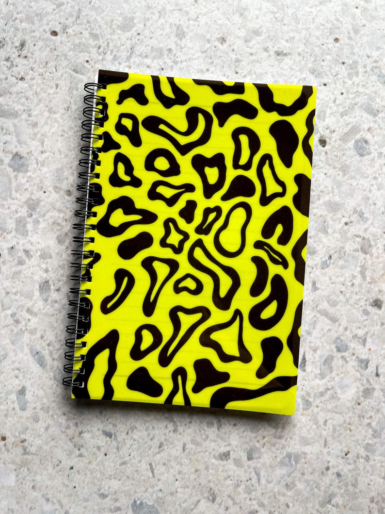 May include: A yellow notebook with a black and white abstract pattern. The notebook has a spiral binding.