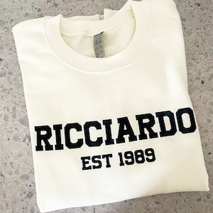 May include: A white t-shirt with black text that reads "RICCIARDO EST 1989".