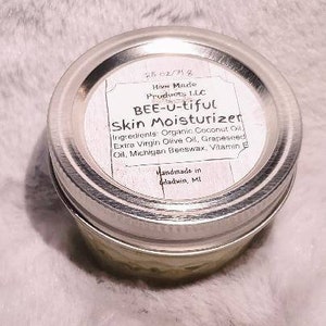 May include: A small glass jar with a silver lid containing a light green skin moisturizer. The label reads "Hive Made Products LLC BEE-U-tiful Skin Moisturizer" and lists the ingredients: Organic Coconut Oil, Extra Virgin Olive Oil, Grapeseed Oil, Michigan Beeswax, Vitamin E. The label also states "Handmade in Gladwin, MI".