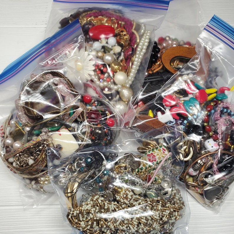 May include: Four clear plastic bags filled with a variety of colorful jewelry, including necklaces, bracelets, earrings, and charms. The jewelry is a mix of beads, metal, and plastic.