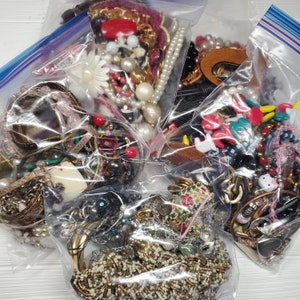 May include: Four clear plastic bags filled with a variety of colorful jewelry, including necklaces, bracelets, earrings, and charms. The jewelry is made of different materials, such as metal, glass, and plastic.