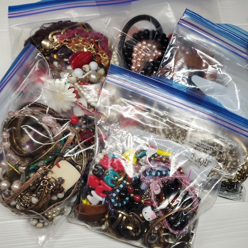 May include: Four clear plastic bags filled with various colorful beads, charms, and jewelry. The bags are sealed with blue zipper closures.