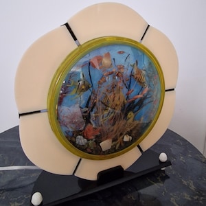 May include: A vintage decorative lamp with a round diorama of an underwater scene, including fish and coral. The cream-coloured, flower-shaped frame has a black base and white accents. The diorama is framed in gold.