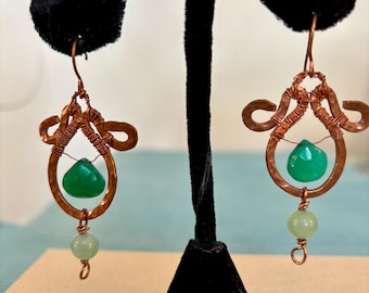 May include: A pair of copper wire earrings with green gemstone accents. The earrings feature a teardrop-shaped green stone, a smaller round green stone, and intricate copper wire designs.