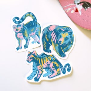 May include: Three colorful animal stickers with a blue, pink, and yellow color scheme. The stickers feature a lemur, a bear, and a tiger.