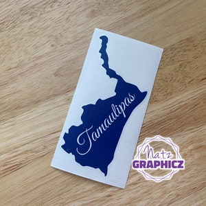 May include: A blue vinyl decal of the state of Tamaulipas, Mexico. The state name is written in white cursive lettering. The decal is on a white background.