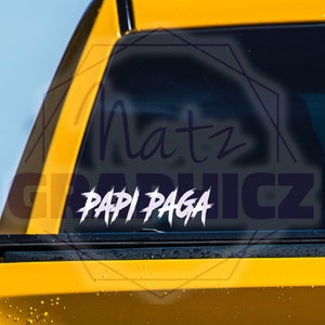 May include: A black and white sticker with the text "Papi Paga" in a stylized font. The sticker is on the back window of a yellow vehicle.