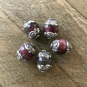 May include: Six round, faceted beads with silver-toned metal accents. The beads are a mix of dark green and burgundy colors.